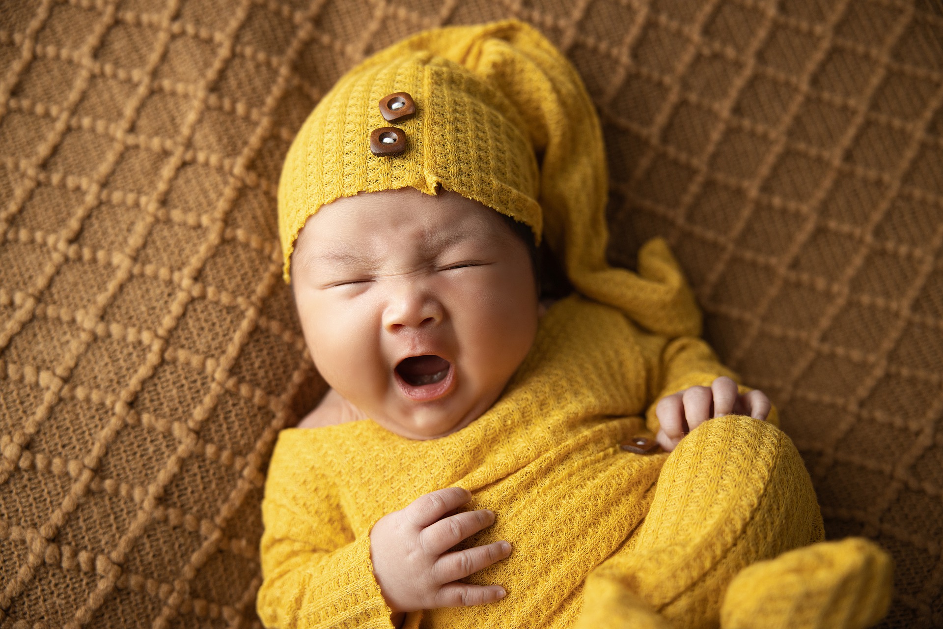 a baby wearing a yellow set of clothes crying